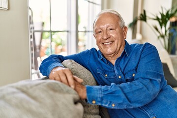 Senior man with grey hair sitting on the sofa at the living room of his house. Mature man smiling happy at home.