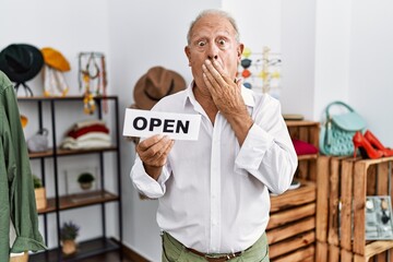 Senior man holding banner with open text at retail shop covering mouth with hand, shocked and afraid for mistake. surprised expression