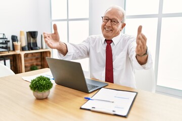 Senior man working at the office using computer laptop looking at the camera smiling with open arms for hug. cheerful expression embracing happiness.