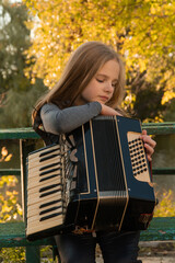 girl playing the accordion in the autumn park. autumn accordion. girl doing music. child in the...