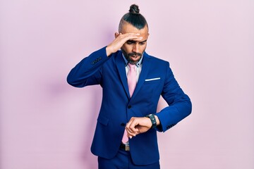 Young hispanic man wearing business suit and tie looking at the watch time worried, afraid of...