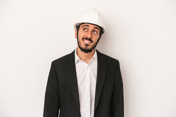 Young architect man wearing a construction helmet isolated on white background dreaming of achieving goals and purposes