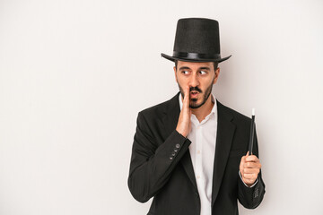 Young magician man holding wand isolated on white background is saying a secret hot braking news and looking aside