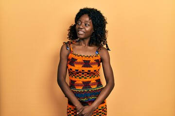 Young african american woman wearing traditional african clothes looking away to side with smile on face, natural expression. laughing confident.