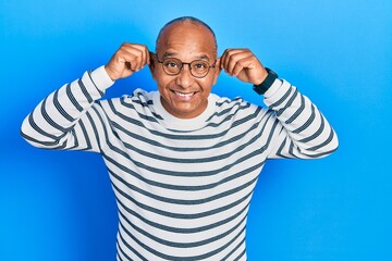 Middle age latin man wearing casual clothes and glasses smiling pulling ears with fingers, funny...
