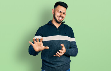 Young hispanic man with beard wearing casual winter sweater disgusted expression, displeased and...