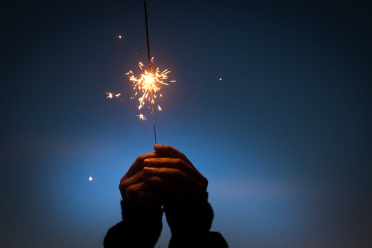 Human hands holding burning fire sparkle. Celebrating new year, christmas or anniversary. Hands holding burning sparkler firework at night. Holiday celebration event