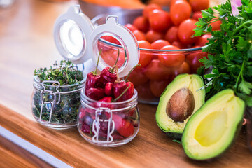 Close up of dried red chillies and herbs in jar with fresh organic vegetables in bowl. Vegetables like tomatoes and cilantro with halved avocado on kitchen counter for preparing food.