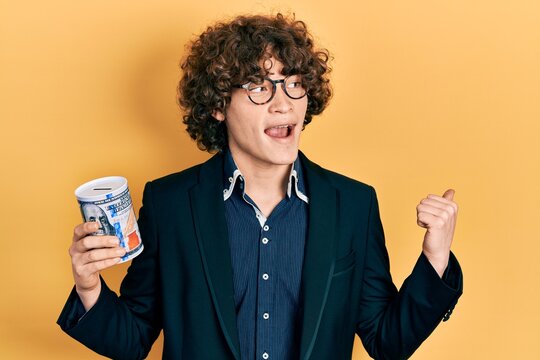 Handsome young man holding piggy bank pointing thumb up to the side smiling happy with open mouth