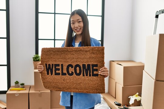 Young chinese girl smiling happy holding welcome doormat at new home
