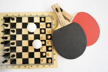 Table tennis rackets in front of a chessboard with pieces and ping pong balls on a white background