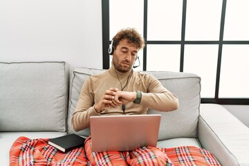 Young handsome man with beard wearing operator headset working from home checking the time on wrist...