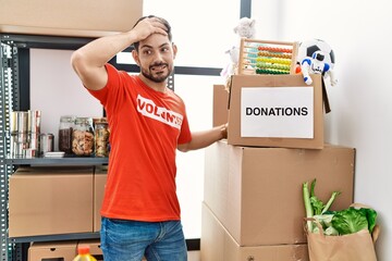 Young man with beard wearing volunteer t shirt at donations stand stressed and frustrated with hand...