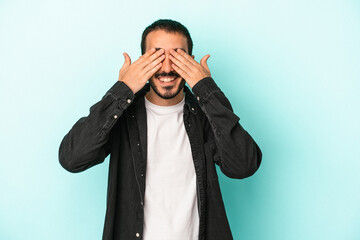 Young caucasian man isolated on blue background covers eyes with hands, smiles broadly waiting for a surprise.