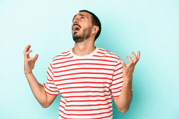 Young caucasian man isolated on blue background screaming to the sky, looking up, frustrated.