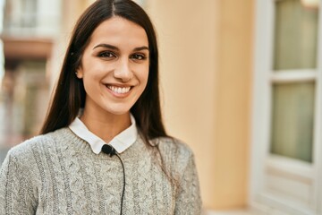 Young hispanic woman smiling happy using microphone tie at the city.
