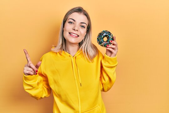 Beautiful caucasian woman holding donut smiling happy pointing with hand and finger to the side