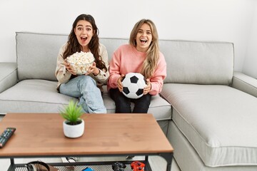 Young couple watching soccer match eating porpcorn at home.