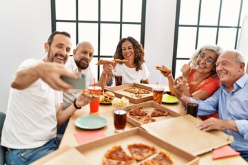 Group of middle age people smiling happy eating italian pizza make selfie by the smartphone at home