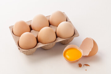 chicken eggs in carton with broken egg and yolk on white background.