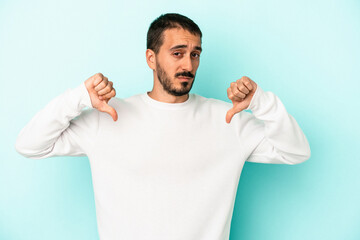 Young caucasian man isolated on blue background showing thumb down, disappointment concept.