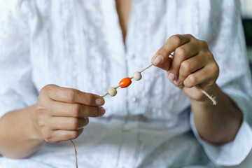 Close up on midsection of unknown female holding string with wooden or plastic pearls making nature...