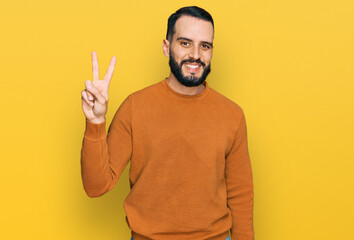 Young man with beard wearing casual winter sweater smiling with happy face winking at the camera doing victory sign. number two.