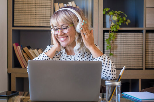 Businesswoman listening music on headphones while working on laptop at home office. Caucasian young woman enjoying music on headphones. Cheerful woman with laptop and headphones at home office
