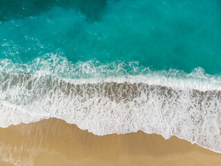 Aerial drone view of waves crushing on tropical beach with sand. Waves breaking on the shore at sunset. Transparent sea water.