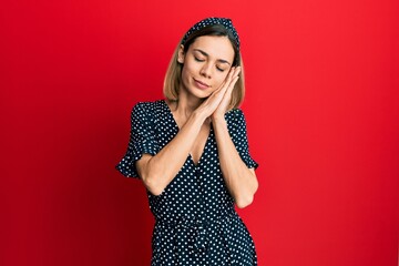 Young caucasian blonde woman wearing beautiful black and white dress sleeping tired dreaming and posing with hands together while smiling with closed eyes.