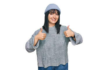 Young hispanic woman wearing cute wool cap success sign doing positive gesture with hand, thumbs up smiling and happy. cheerful expression and winner gesture.