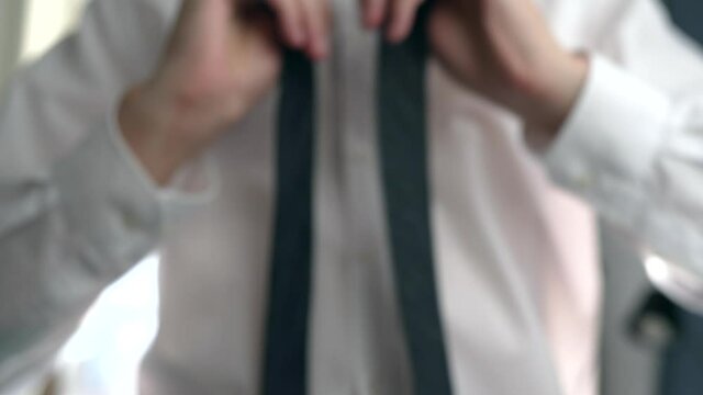 The young man takes out clothes from the wardrobe, puts on a suit and ties a tie in front of the mirror