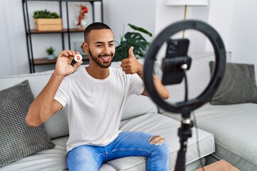 African american man recording vlog tutorial about bitcoin with smartphone at home smiling happy and positive, thumb up doing excellent and approval sign