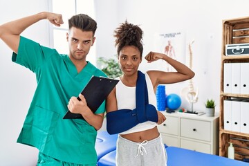 Physiotherapist working with patient wearing arm on sling at rehabilitation clinic strong person...
