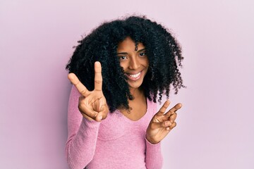 African american woman with afro hair wearing casual pink shirt smiling looking to the camera showing fingers doing victory sign. number two.
