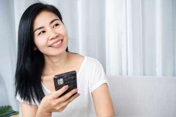 smiling Asian woman using a smartphone, thinking and daydreaming of something with happy face