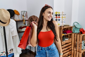 Young brunette woman holding shopping bags at retail shop looking away to side with smile on face, natural expression. laughing confident.