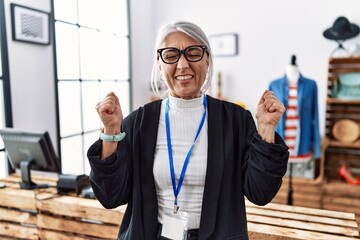 Middle age grey-haired woman working as manager at retail boutique excited for success with arms raised and eyes closed celebrating victory smiling. winner concept.