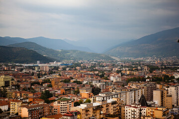 Aerial view of the mountains and  the modern centre of Brescia (Lombardy, Italy) with tiled red roofs, chimneys, cathedral's domes and tall white brick old towers. Traditional European architecture.