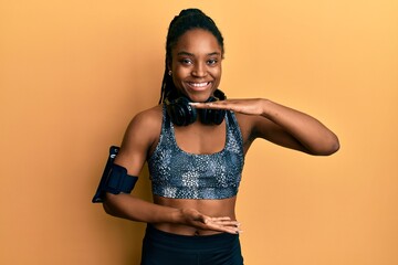 African american woman with braided hair wearing sportswear and arm band gesturing with hands showing big and large size sign, measure symbol. smiling looking at the camera. measuring concept.