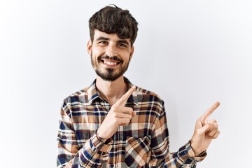 Fototapeta premium Hispanic man with beard standing over isolated background smiling and looking at the camera pointing with two hands and fingers to the side.