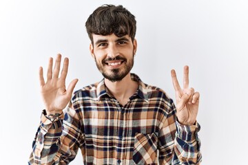 Hispanic man with beard standing over isolated background showing and pointing up with fingers number seven while smiling confident and happy.