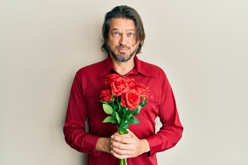Middle age handsome man holding bouquet of red roses puffing cheeks with funny face. mouth inflated with air, catching air. - obrazy, fototapety, plakaty