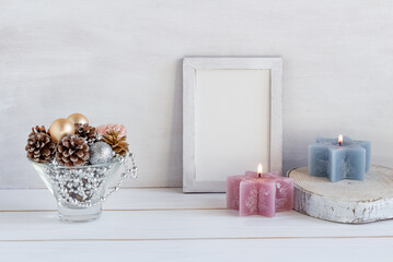 Fototapeta na wymiar Christmas decoration, mock up in a white frame with cones and new year beads, candles on a white table, copy space