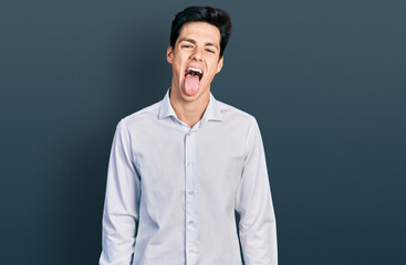 Young hispanic business man wearing business clothes sticking tongue out happy with funny expression. emotion concept.