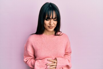 Young brunette woman with bangs wearing casual winter sweater with hand on stomach because indigestion, painful illness feeling unwell. ache concept.