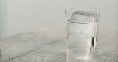 clear ice cube in tumbler glass with tonic on black oak table