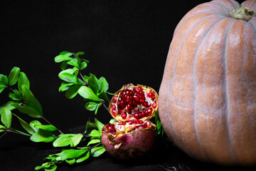 pumpkin and red pomegranate and seeds with green leaves on wooden old cutting board, side view, dark background