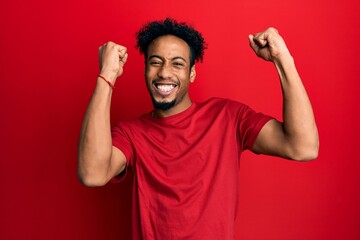 Young african american man with beard wearing casual red t shirt celebrating surprised and amazed...