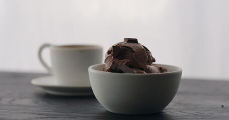 put chocolate pieces on chocolate ice cream into white bowl with espresso on black wood table